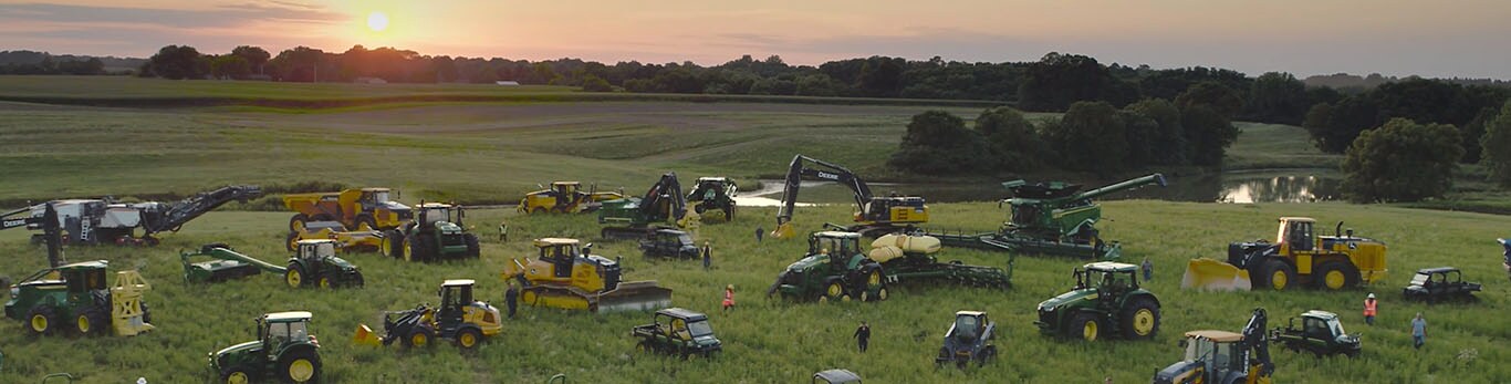 Mennesker, der går blandt flere typer John Deere udstyr på en stor mark.