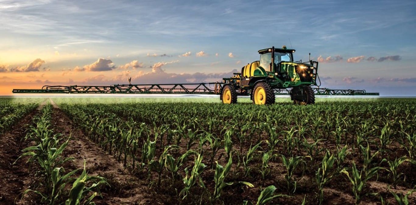 John Deere sprøjte arbejder på en majsmark med solnedgangen i baggrunden