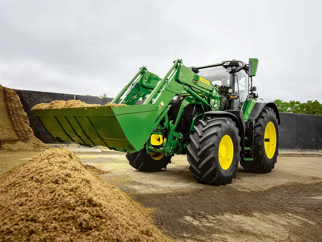 Frontlæsserskovl fyldt med ensilage på en John Deere traktor under materialehåndteringsarbejde.