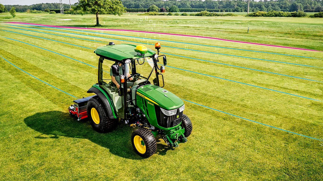 En greenkeeper arbejder på et græsområde med en John Deere-kompakttraktor.