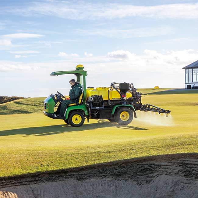 En greenkeeper arbejder på et græsområde med en John Deere-sprøjte