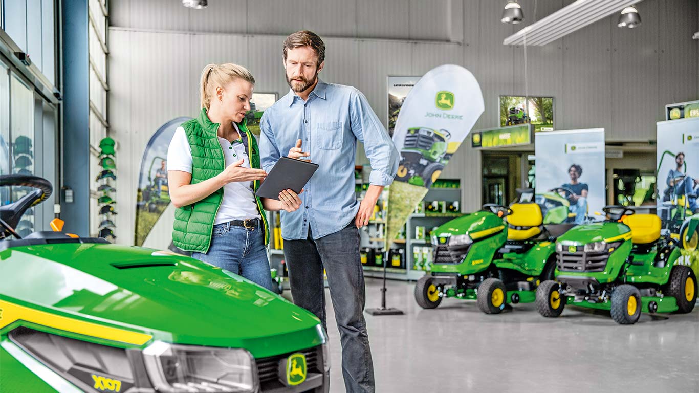 En John Deere-forhandler rådgiver en kunde om køb af en John Deere-plæneklipper.