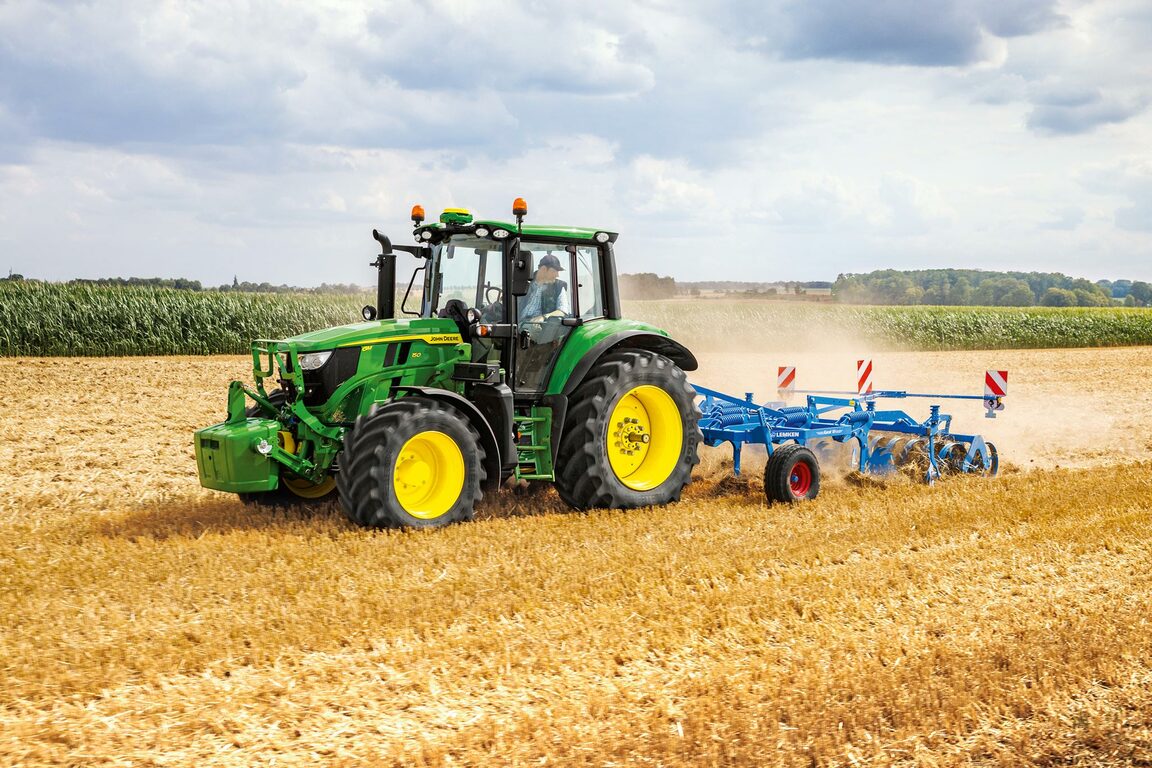 John Deere traktor, der trækker en blå kultivator hen over en tør mark og forbereder jorden til plantning