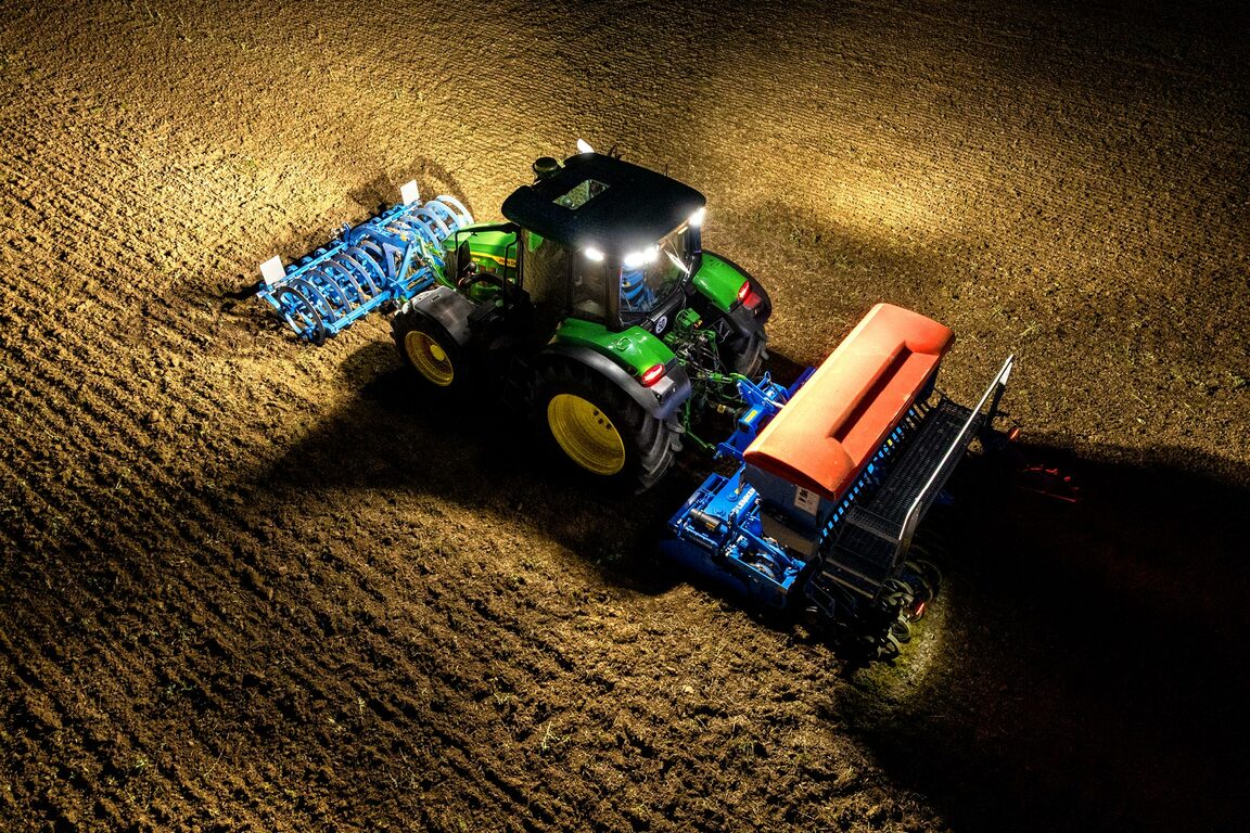 John Deere traktor, der kører om natten med oplyst såudstyr på en opdyrket mark