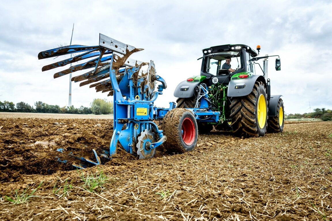 John Deere traktor pløjning af jord med en blå vendbar plov på en høstet mark