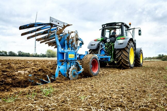 John Deere traktor pløjning af jord med en blå vendbar plov på en høstet mark