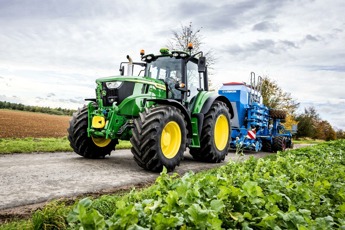 John Deere traktor, der trækker en blå præcisionssåmaskine langs et landbrugsspor ved siden af afgrøder