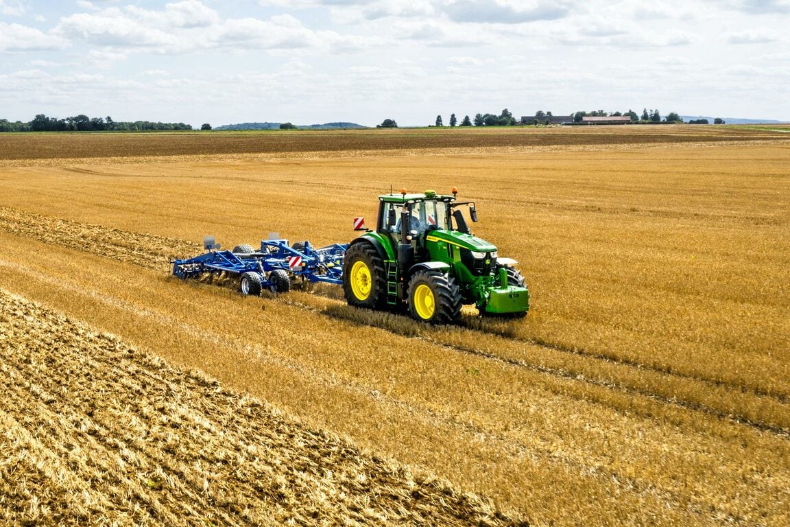 En John Deere-traktor, der bearbejder en stor åben mark med et blåt jordbearbejdningsredskab