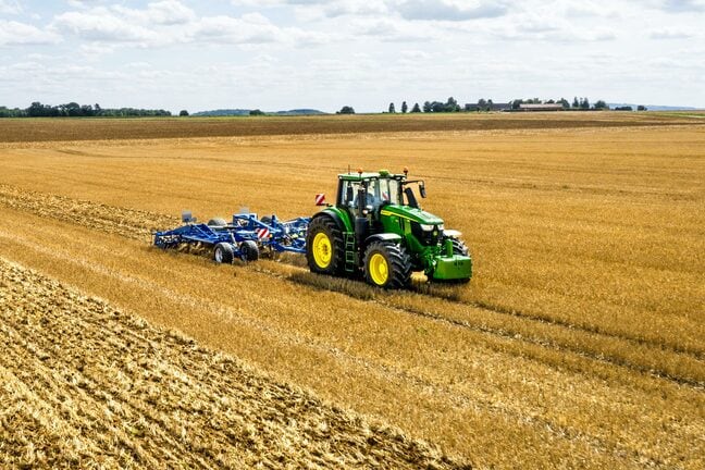 En John Deere-traktor, der bearbejder en stor åben mark med et blåt jordbearbejdningsredskab