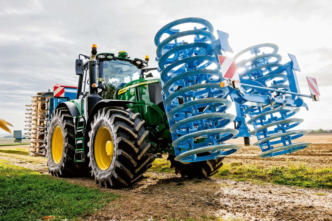 En John Deere-traktor, der står parkeret med sammenklappede blå kultivatorskiver på en mark efter markarbejdet