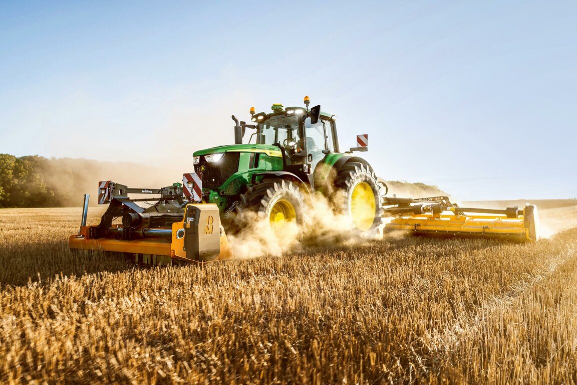 En John Deere-traktor, der findeler afgrøderester med en bred bagmonteret findeler på en mark