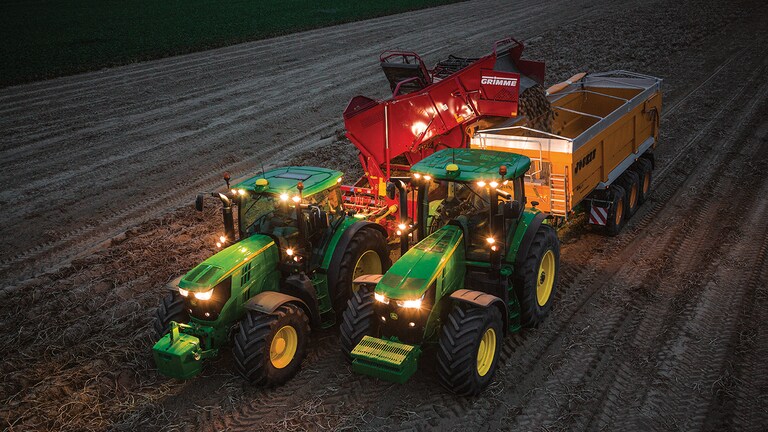 Traktor der tr&aelig;kker kartoffelh&oslash;ster om natten og afl&aelig;sser kartofler til en vogn der er trukket af en anden traktor