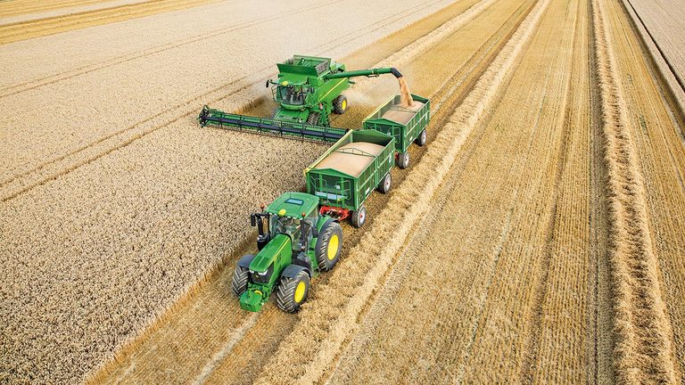 John Deere S-Series mejet&aelig;rsker der afl&aelig;sser hvede i to trailere trukket af en traktor