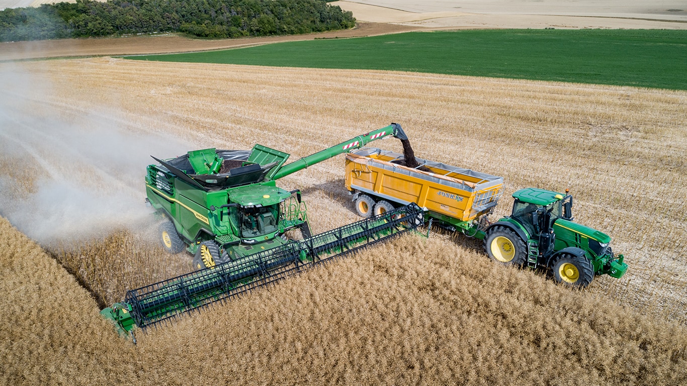 John Deere X-Series mejet&aelig;rsker der afl&aelig;sser rasp i en kornvogn trukket af en John Deere traktor