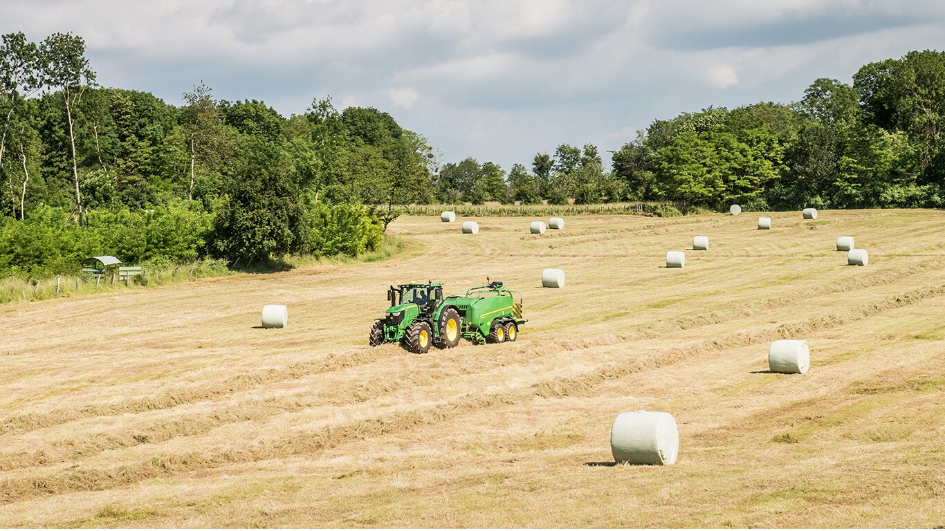 John Deere traktor med ballepresser på marken med ensilageballer