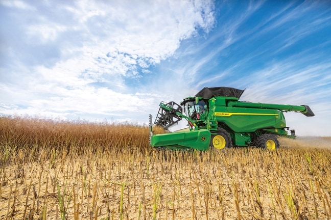 John Deere-mejetærsker høster korn med skærebord på marken under blå himmel under afgrødehøst