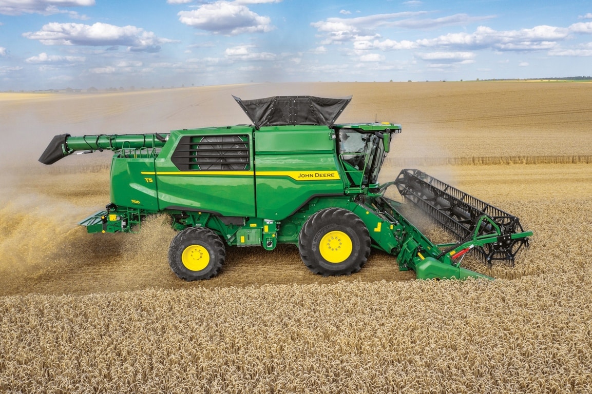 John Deere-mejetærsker med skærebord, der høster hvede på stor landbrugsmark, set fra siden