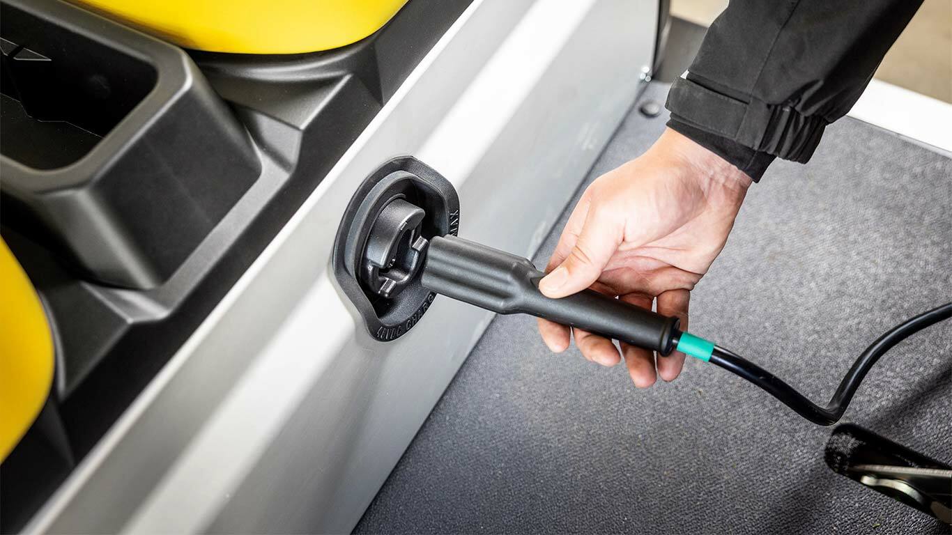 Hånd, der slutter et opladningskabel til sideporten på en John Deere Gator GS elektrisk transporter.