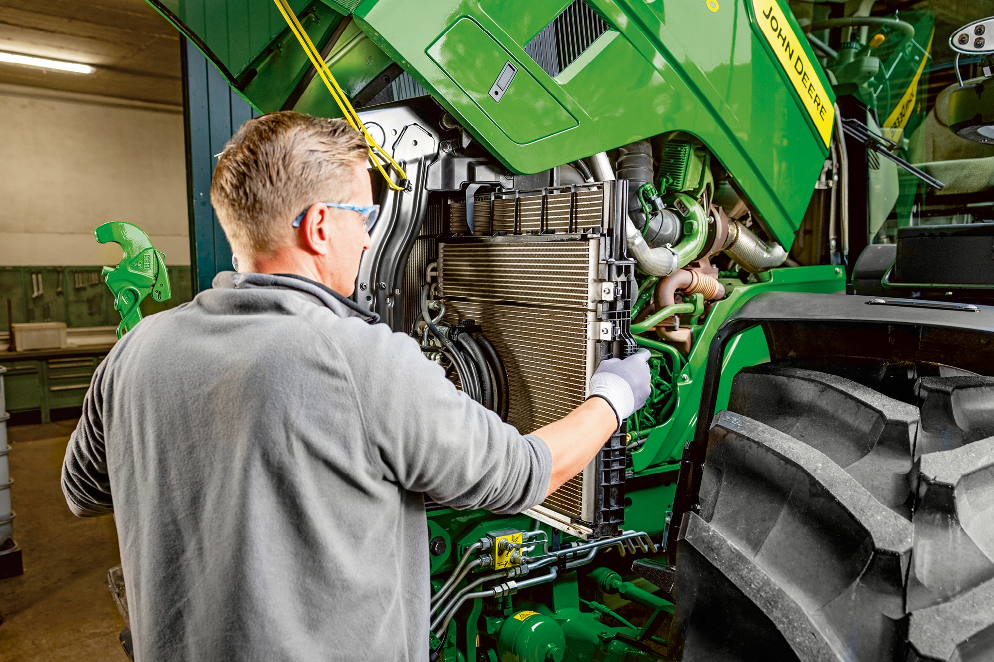 En servicetekniker udfører vedligeholdelse i motorrummet på en traktor fra John Deere 6M-serien.