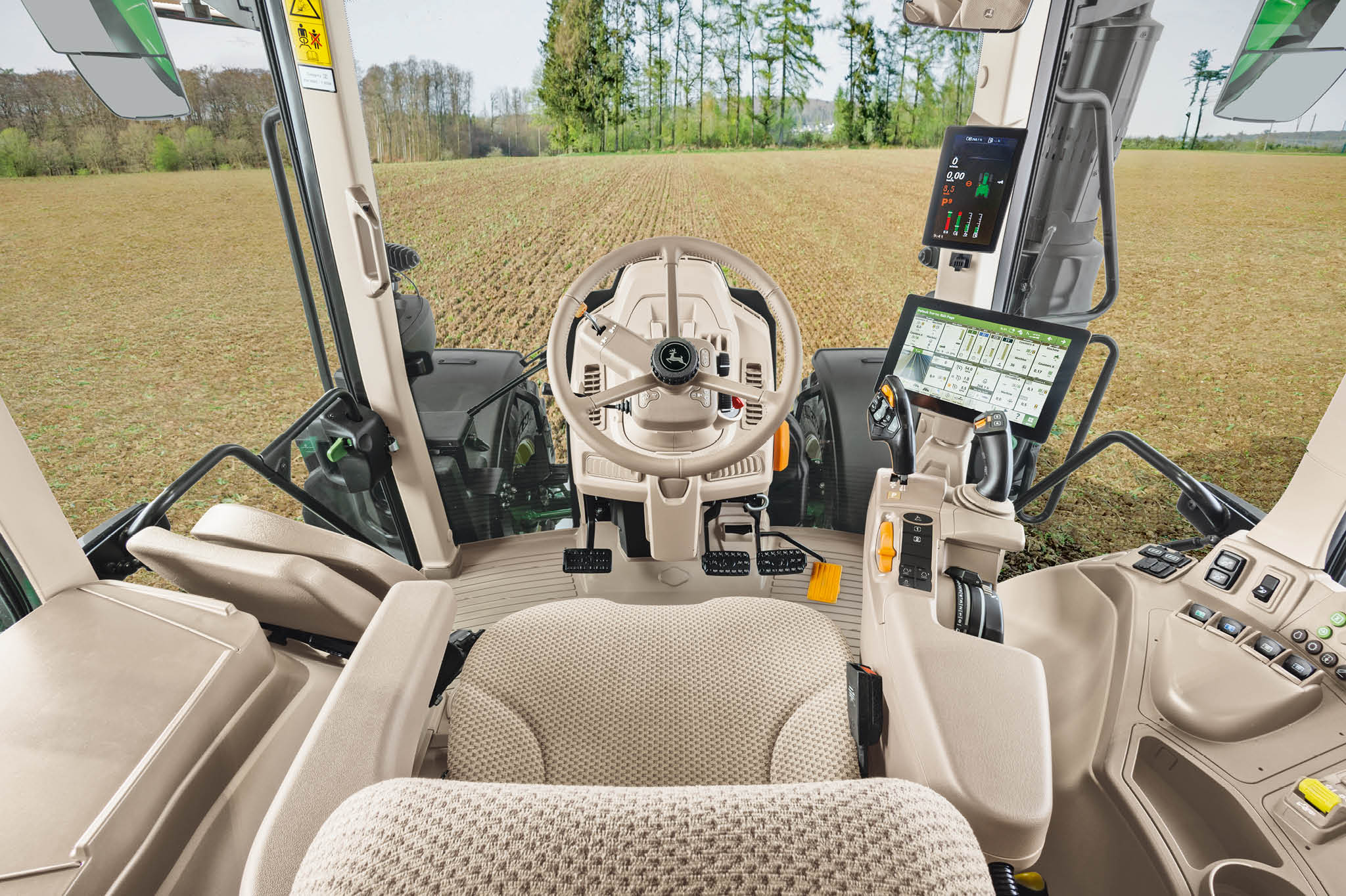 Oversigt over kabinen i en John Deere 6M-serie traktor med førersæde, rat og digitale skærme.