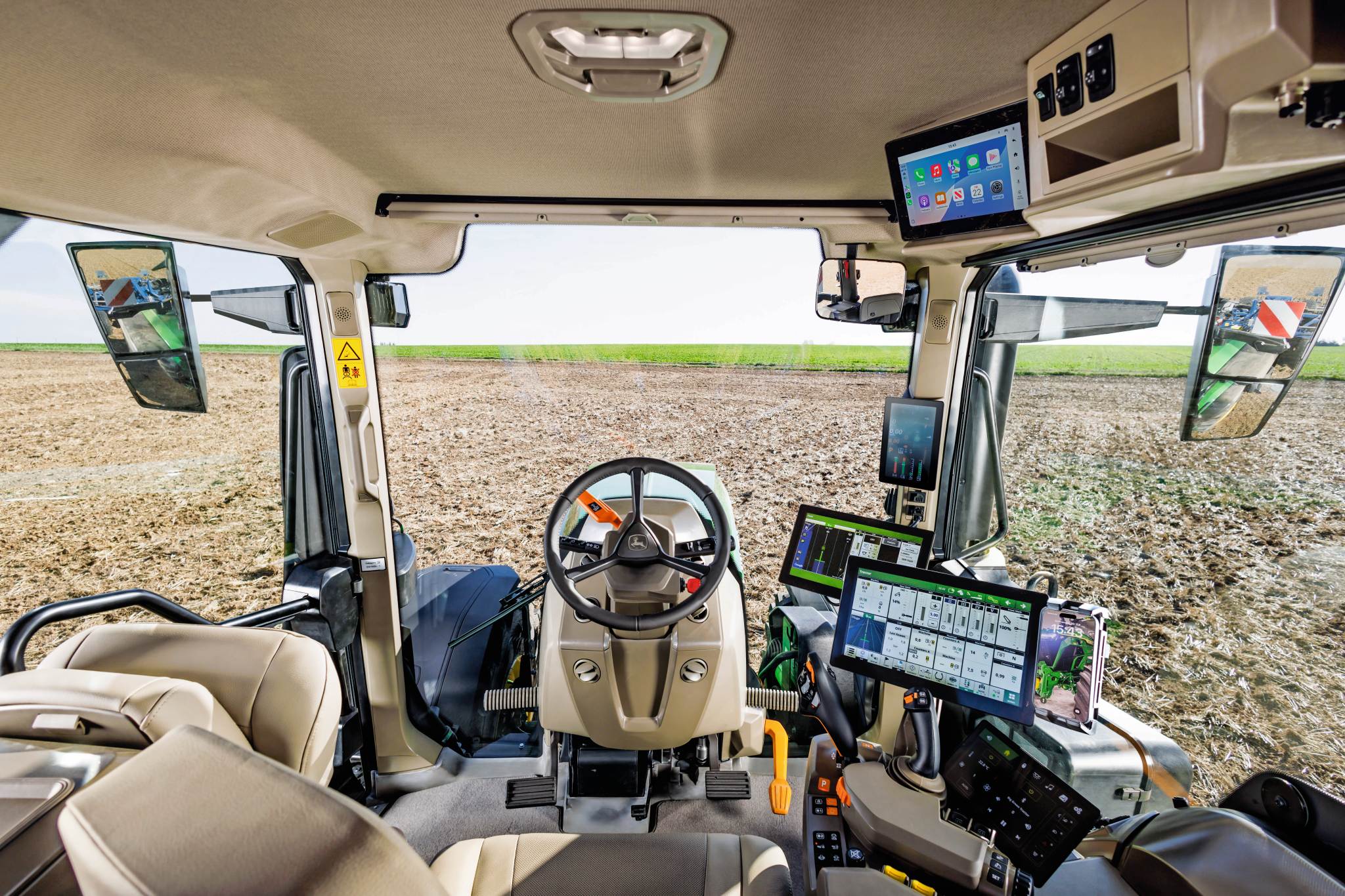 Et moderne traktor-kabineinteriør med rat, touchscreen-skærme og betjeningsknapper til præcisionslandbrug med udsigt over en dyrket mark