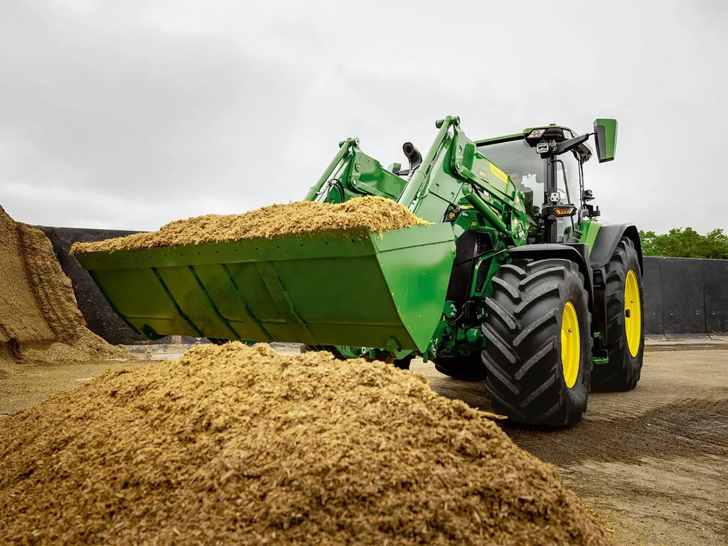 John Deere traktor med frontlæsser til transport af snittet ensilage på et landbrugslager.