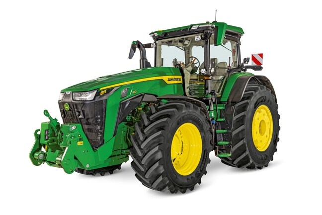 John Deere 8R traktor med lukket førerhus, store landbrugsdæk og frontlift, vist på en hvid studiobaggrund.