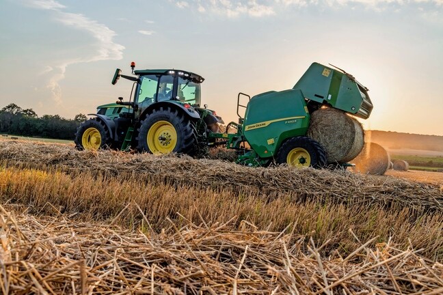 John Deere F442M ballepresser trukket af en John Deere 6M-traktor, der udstøder en halmballe