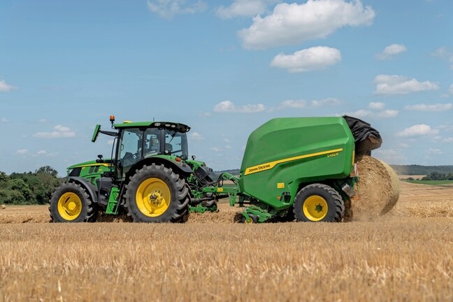 John Deere V452R på en halmmark trukket af en John Deere 6R 150, der udstøder en balle