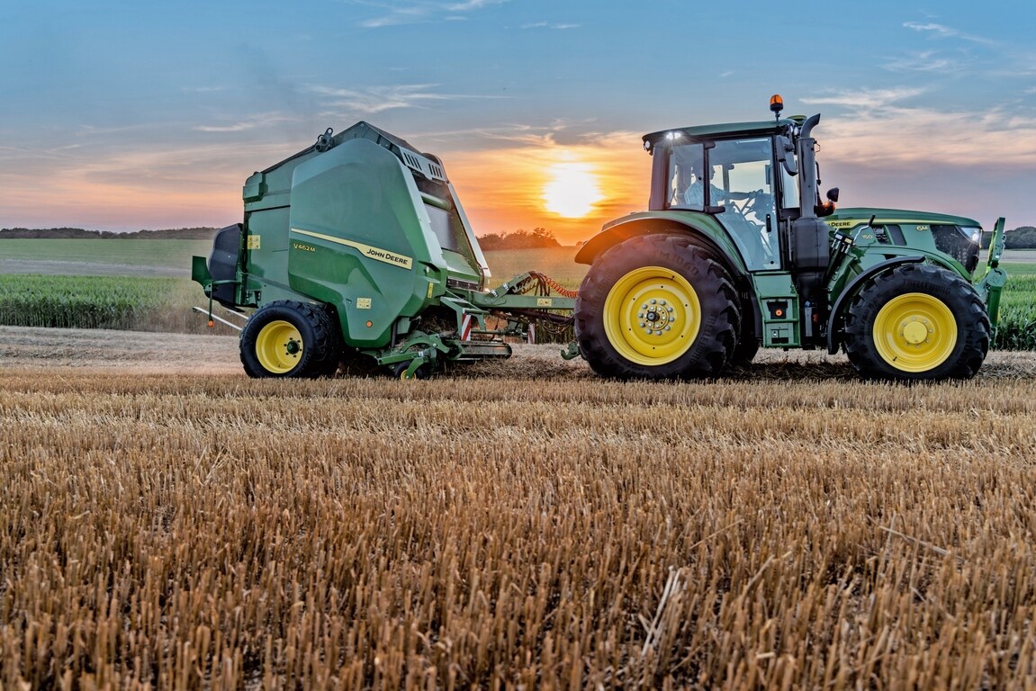John Deere V462M på en halmmark trukket af en John Deere 6M 150 ved solnedgang