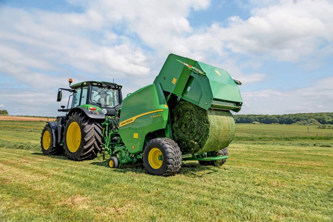 John Deere F442M-ballepresser trukket af en John Deere 6M-traktor, der udstøder en græsballe