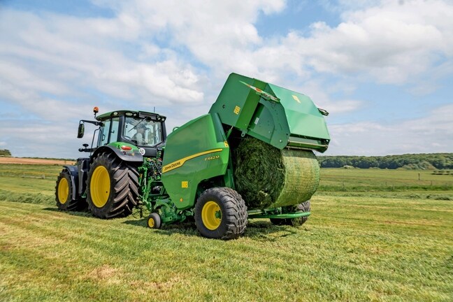 John Deere F442M-ballepresser trukket af en John Deere 6M-traktor, der udstøder en græsballe