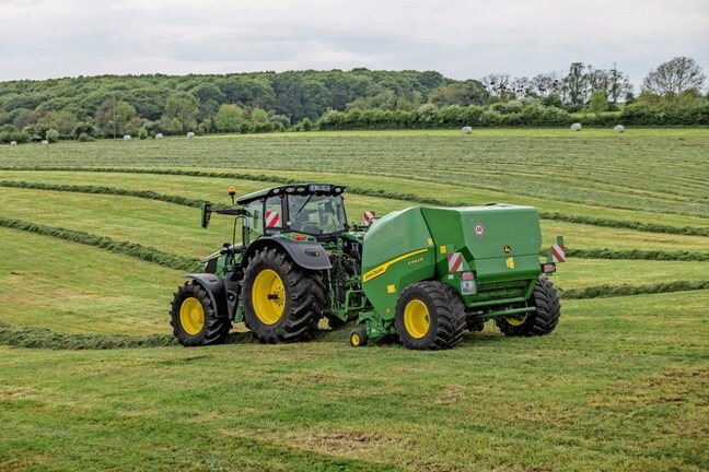 John Deere F442R-ballepresser trukket af en John Deere 6M-traktor på en kuperet græsmark