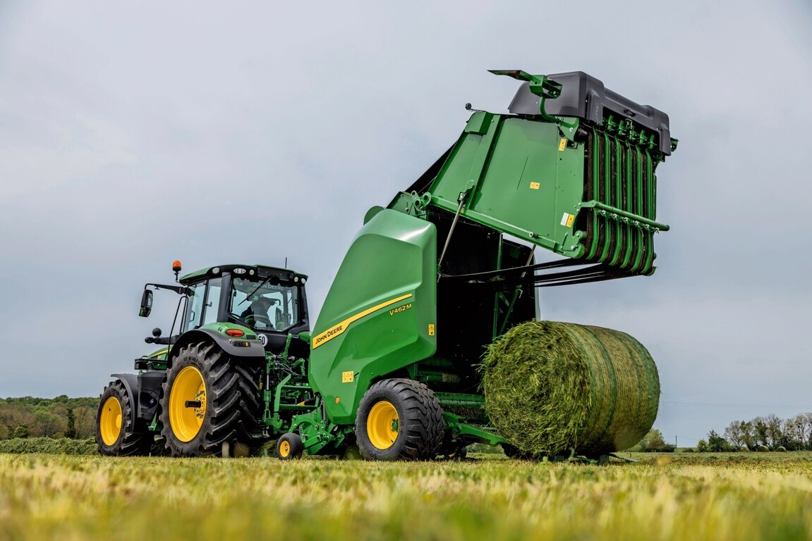 John Deere V462M-ballepresser trukket af en John Deere 6M-traktor, der udstøder en græsballe