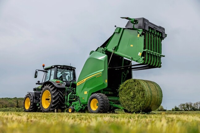 John Deere V462M-ballepresser trukket af en John Deere 6M-traktor, der udstøder en græsballe